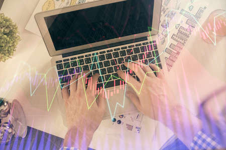 Double exposure of mans hands typing over laptop keyboard and forex chart hologram drawing. Top...