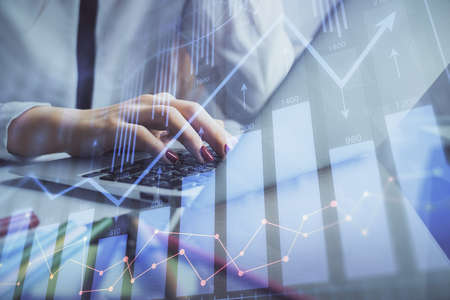 Double exposure of woman hands typing on computer and financial graph hologram drawing. Stock market...