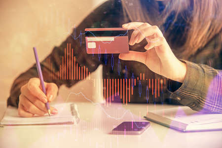 Double exposure of woman on-line shopping holding a credit card and financial graph drawing. Stock...
