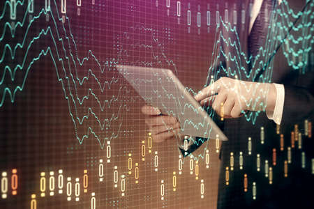 Double exposure of mans hands holding and using a digital device and forex graph drawing. Financial...