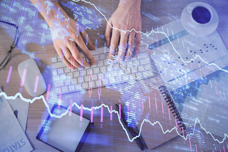 Multi exposure of mans hands typing over computer keyboard and forex graph hologram drawing. Top...