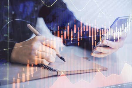 Double exposure of forex graph sketch hologram and woman holding and using a mobile device. Stock...