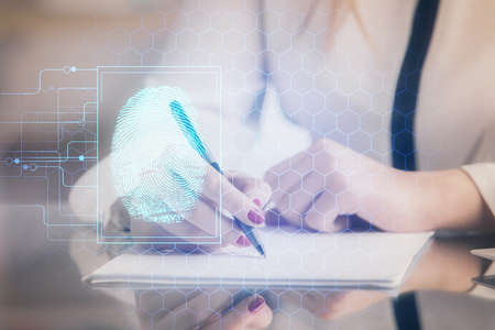 Blue fingerprint hologram over womans hands taking notes background. Concept of protection. Double exposureの写真素材