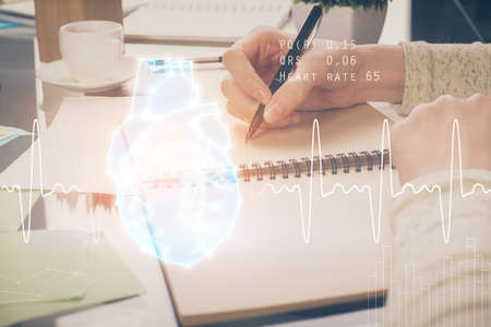 Heart hologram over womans hands writing background. Concept of Medical study. Multi exposureの写真素材