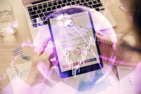 Double exposure of mans hands holding and using a digital device and forex graph drawing. Financial...