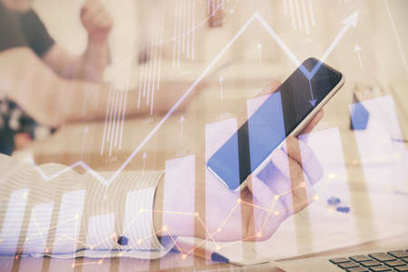 Double exposure of mans hands holding and using a digital device and forex graph drawing. Financial...