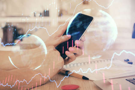 Double exposure of mans hands holding and using a digital device and forex graph drawing. Financial...