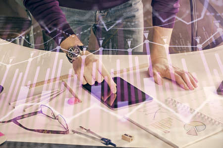 Double exposure of mans hands holding and using a digital device and forex graph drawing. Financial...
