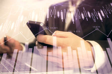 Multi exposure of mans hands holding and using a digital phone and forex graph drawing. Financial...