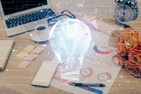 Computer on desktop in office with bulb icon hologram. Double exposure. Concept of idea.
