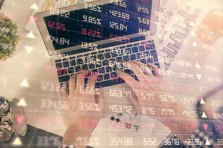 Double exposure of mans hands typing over laptop keyboard and forex chart hologram drawing. Top...