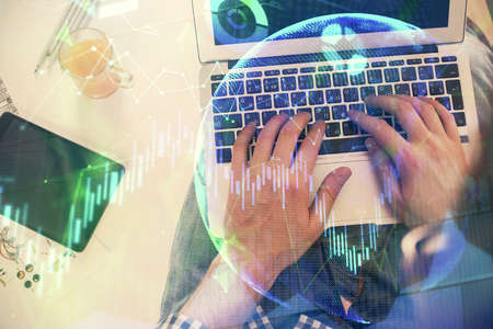 Double exposure of mans hands typing over laptop keyboard and forex chart hologram drawing. Top...