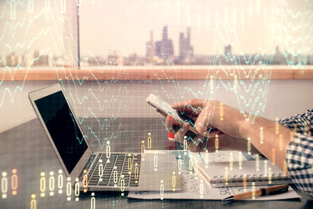 Double exposure of mans hands holding and using a digital device and forex graph drawing. Financial...