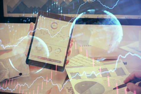 Double exposure of mans hands holding and using a digital device and forex graph drawing. Financial...