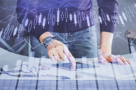 Double exposure of mans hands holding and using a digital device and forex graph drawing. Financial...