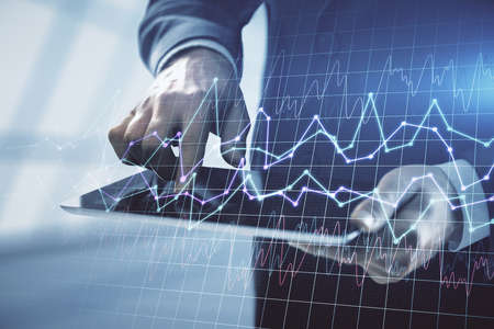 Double exposure of mans hands holding and using a digital device and forex graph drawing. Financial...