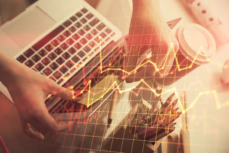 Double exposure of businesswoman hands typing on computer and financial graph hologram drawing....