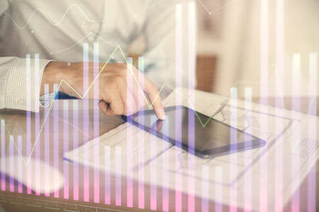 Double exposure of mans hands holding and using a digital device and forex graph drawing. Financial...