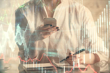 Double exposure of financial graph sketch hologram and woman holding and using a mobile device....