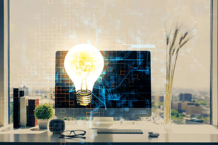 Computer on desktop in office with bulb icon hologram. Double exposure. Concept of idea.の写真素材