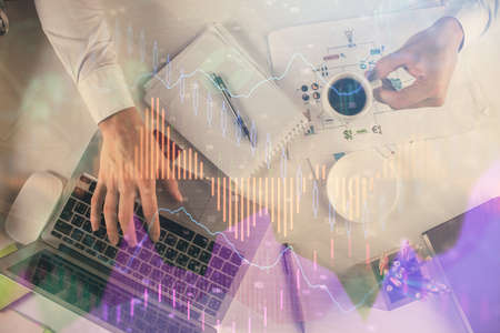 Multi exposure of mans hands typing over computer keyboard and forex graph hologram drawing. Top...