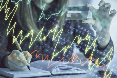 Double exposure of woman on-line shopping holding a credit card and financial graph drawing. Stock...