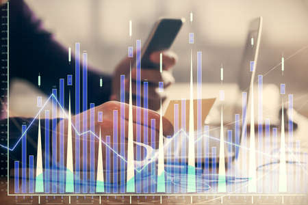 Double exposure of mans hands holding and using a phone and financial graph drawing. Analysis concept.の写真素材