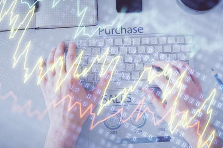 Double exposure of mans hands typing over laptop keyboard and forex chart hologram drawing. Top...
