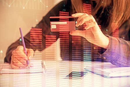 Double exposure of woman on-line shopping holding a credit card and financial graph drawing. Stock...