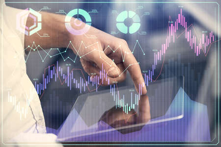 Double exposure of mans hands holding and using a digital device and forex graph drawing. Financial...