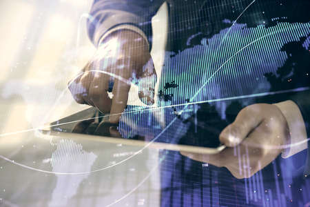 Double exposure of mans hands holding and using a digital device and forex graph drawing. Financial...