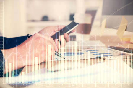 Double exposure of mans hands holding and using a phone and financial graph drawing. Analysis...