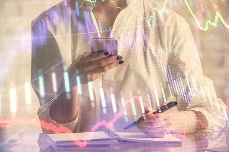 Double exposure of financial graph sketch hologram and woman holding and using a mobile device....