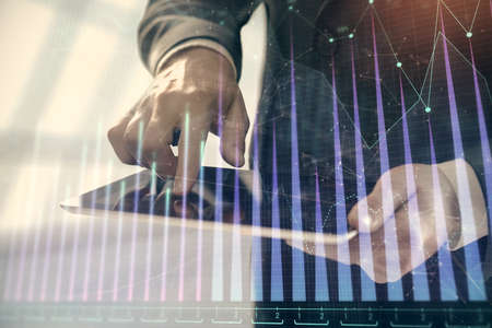 Double exposure of mans hands holding and using a digital device and forex graph drawing. Financial...