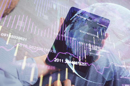 Double exposure of mans hands holding and using a digital device and forex graph drawing. Financial...