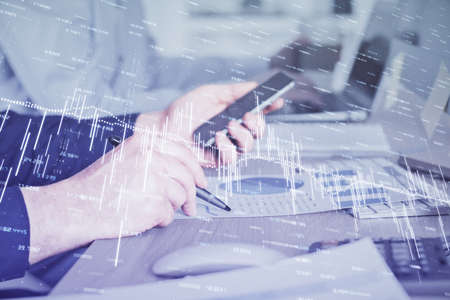 Double exposure of mans hands holding and using a digital device and forex graph drawing. Financial...