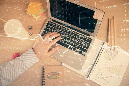 Double exposure of mans hands typing over computer keyboard and forex graph hologram drawing. Top view. Financial markets concept.の写真素材