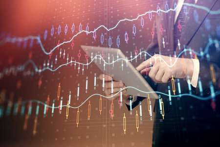 Double exposure of mans hands holding and using a digital device and forex graph drawing. Financial...