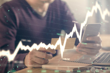Double exposure of mans hands holding and using a phone and financial graph drawing. Analysis...