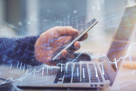 Double exposure of mans hands holding and using a phone and financial graph drawing. Analysis...