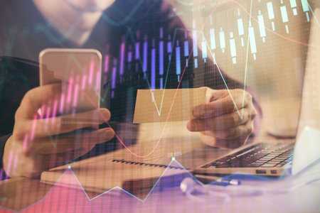 Double exposure of mans hands holding and using a phone and financial graph drawing. Analysis...