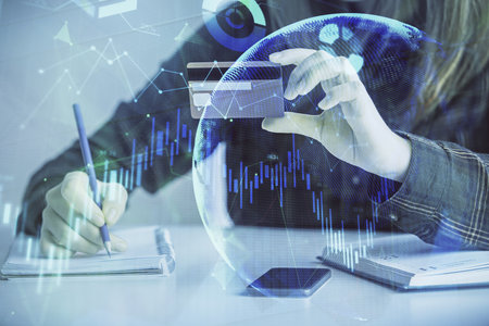 Double exposure of woman on-line shopping holding a credit card and financial graph drawing. Stock...
