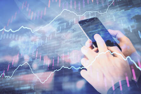 Double exposure of mans hands holding and using a digital device and forex graph drawing. Financial...
