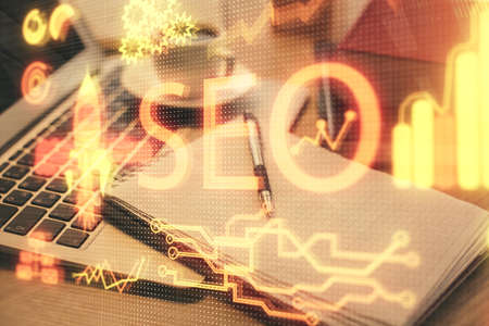 Double exposure of SEO writing and desktop with coffee and items on table background. Concept of search optimization.の写真素材