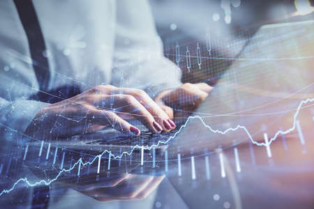 Double exposure of businesswoman hands typing on computer and financial graph hologram drawing....