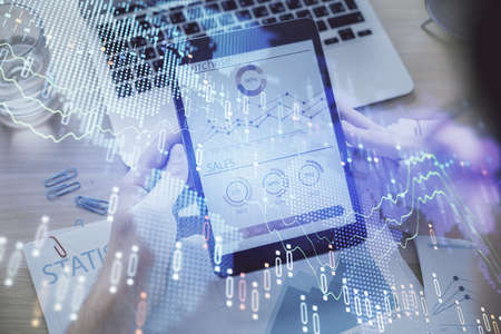 Double exposure of mans hands holding and using a digital device and forex graph drawing. Financial...
