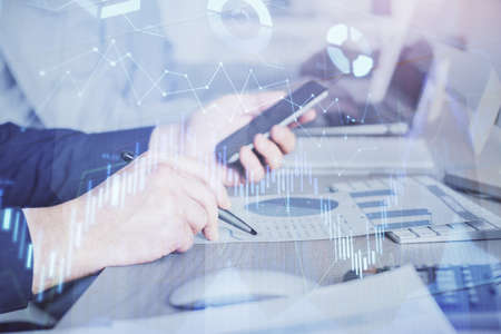 Double exposure of mans hands holding and using a digital device and forex graph drawing. Financial...