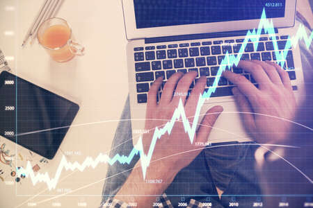 Double exposure of mans hands typing over laptop keyboard and forex chart hologram drawing. Top...