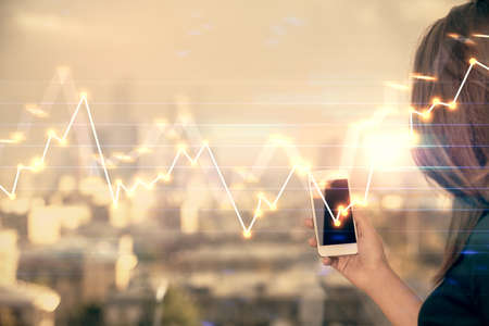 Double exposure of forex chart sketch hologram and woman holding and using a mobile device. Stock...