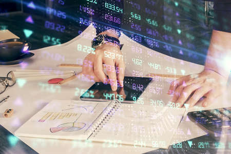 Double exposure of mans hands holding and using a digital device and forex graph drawing. Financial...